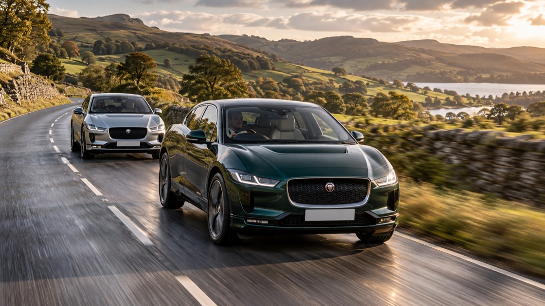 Two right-hand-drive I-PACE-style cars travelling together in the left-hand lane through the British countryside.